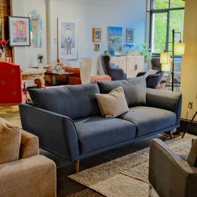 A modern sofa in the center of an interior design store, surrounded by various furniture and decor items, such as accent chairs.