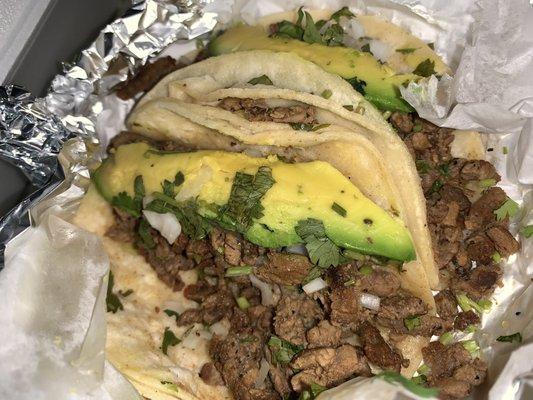 Beef Fajita Tacos with white cheese, onion, cilantro, avocado, green salsa, and lime.