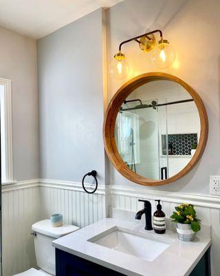 Blue single vanity with round natural wood color and black and gold scone light.