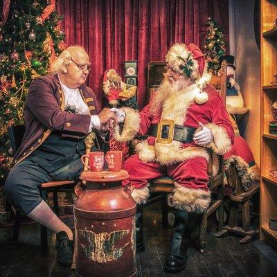 Saint Nick and Ben Franklin having some hot cocoa in Santa's workshop.