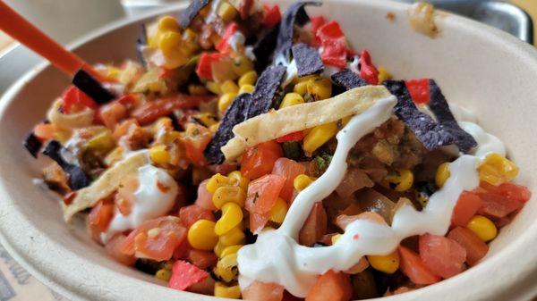 Bowl with cauliflower rice, dark meat chicken, extra roasted corn and peppers topped with sour cream and tortilla strips