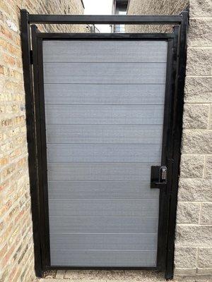 Custom fabricated pedestrian gate in alley , made from European green wood and locking keypad .