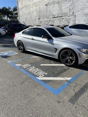 A silver car is parked horizontally across a handicapped parking spot