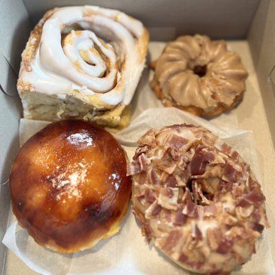 Clockwise, from top left - Cinnamon Roll, Maple Cruller, Maple Bacon Donut, and a Crème Brûlée Donut.