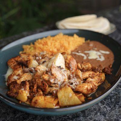 Chacalele - grilled chicken mixed with chorizo & pineapple then drizzled in queso dip, accompanied by a side of rice, beans & warm tortillas