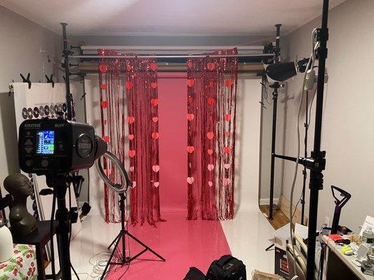 Valentine Photoshoot: pink on white backdrop with hanging red hearts and red tinsel curtains.