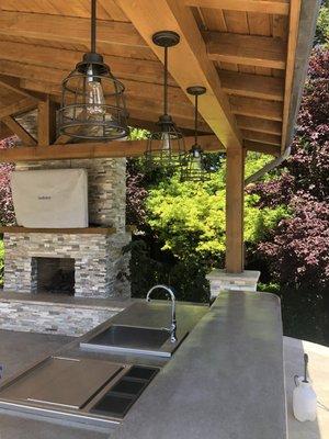 Covered roof over a beautiful fireplace and outdoor kitchen. Both fireplace and islands are faced with stone veneer.