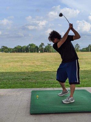 One of the covered golf mats to hit from. You'll see a large open field in the background.