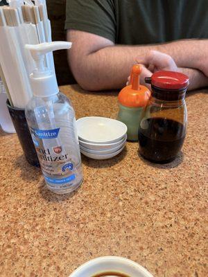 Table stocked with straws, chopsticks, hand sanitizer, soy sauce, wasabi and dipping dishes.