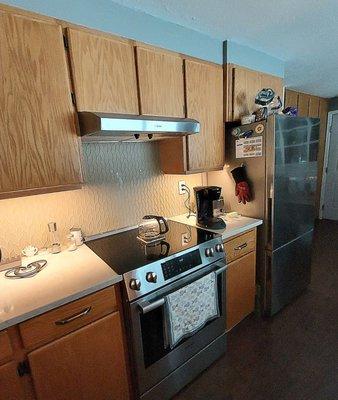 New range, range hood, fridge, countertops, backsplash and undercabinet lights in kitchen