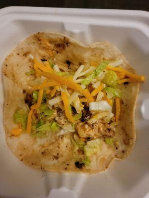 A shrimp taco with one piece of chopped up cold shrimp on a stale tortilla with wilted lettuce and a little cheese