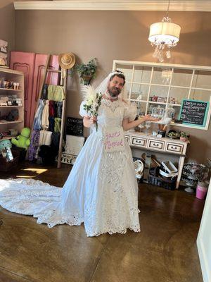 "A Bride in His Element!" - Mitch striking a pose inside the cozy bakery, showing off his gown and bouquet, clearly enjoying the attention.