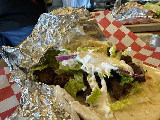 This is how the restaurant presents the gyros , notice the dark grilled to kill meat underneath the sloppy topping.