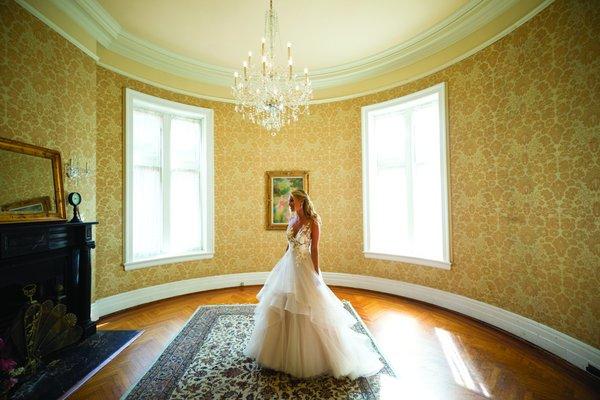 In the grandeur of her private suite, the bride basks in a moment of serene beauty, illuminated by the soft glow of a magnificent chandelier