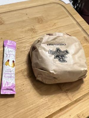 Unwrapped cheeseburger with drink packet for scale.