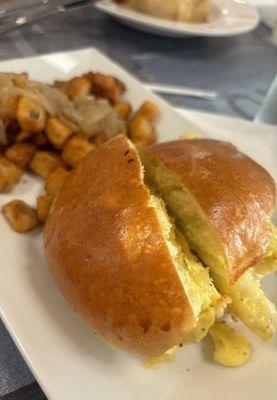 Egg sandwich with pepperjack cheese, brioche bun, and seasoned potatoes with caramelized onions