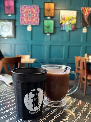 Hot cocoa and water in foreground. Original art in the background.