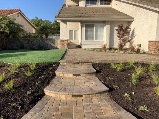 Turf, rustic wall, stacked stone columns, paver driveway and front entry, plants, lights, drip, stucco