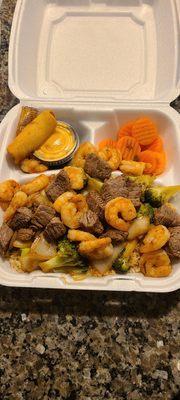 Steak and shrimp meal with a  spring roll and sweet carrots.