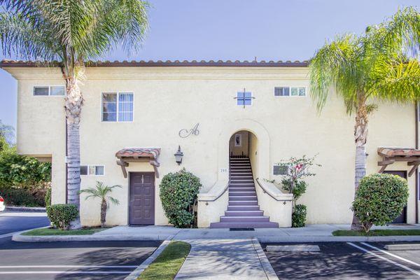 front exterior view of The Village Apartments with staircase and palm trees.