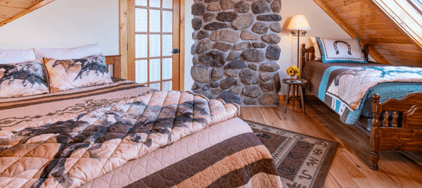 Queen and twin bed aside a large stone chimney with horse motif blankets.