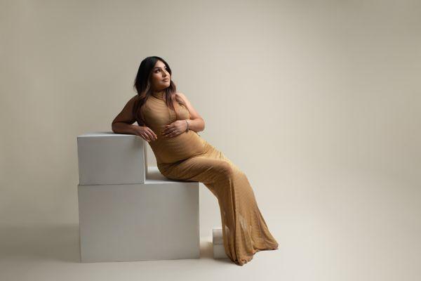 Expectant mom in gold dress lounging on white boxes