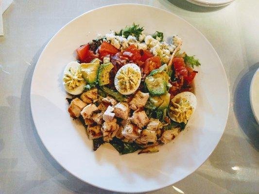 Deviled egg cobb salad with romaine and greens tossed with herbed buttermilk dressing and topped with avocado, grilled basil chicken, bacon.