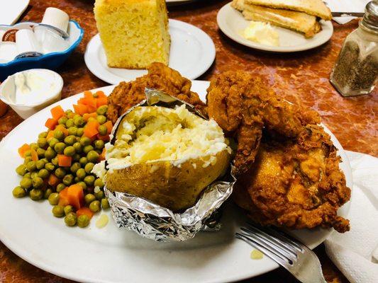 Fried chicken with a baked potato and peas and carrots with cornbread.