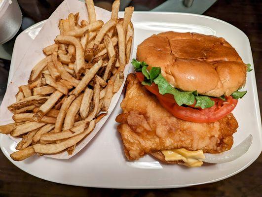 Sizeable fish sandwich with fries.