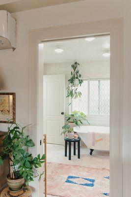 A scene from a former project--open concept bathroom featuring a claw foot tub with plants lining the space.