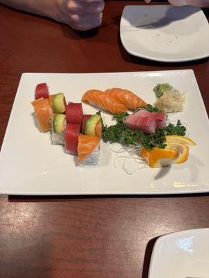 Rainbow Roll on the left, salmon sushi at the top and yellow tail sitting on top of the kale