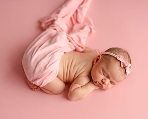 baby girl chin on hands on pink backdrop