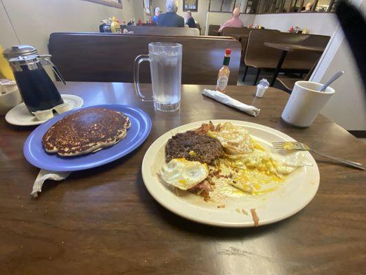 Chopped steak with eggs, hash brown and pancake with a coffee and water.