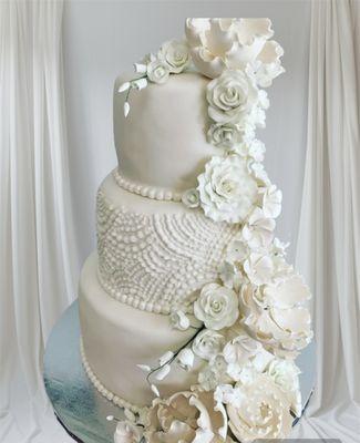 This is an elegant three-tiered cake in white tones, decorated with detailed pearl and sugar flowers