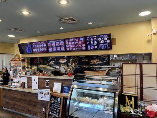 Front counter, digital menu, & specials on a wooden stand. Pickled sides in a refrigerated case.  There is a wide selection of beverages.