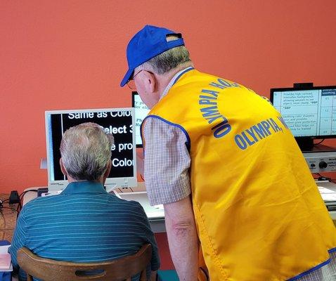 man in lion's vest assisting low vision client at reading machine