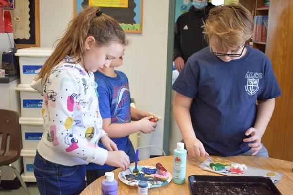 A girl and a boy painting clay sculptures.