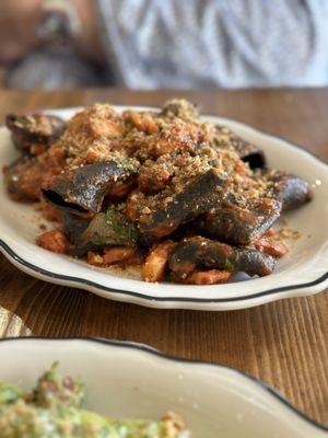 Squid ink paccheri: Fresh DPNB Squid ink Paccheri served with octopus ragu (tomato, olives, Aleppo, & oregano), topped with breadcrumbs.