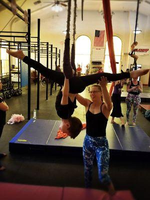 aerial instructor holly dison spotting one of our youth aerial students through training on the trapeze