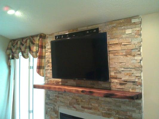 Another TV mounted over a fireplace with a soundbar and concealed wiring.