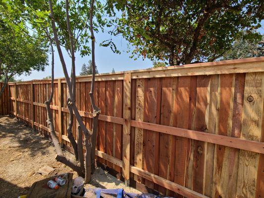 Back of a redwood fence with redwood rails and metal posts hidden.