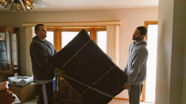 Quinn and Anthony carrying a wrapped dresser.