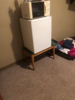 Discolored microwave and fridge with ice compartment covered in ice.  Sitting on and old bench that, frankly is needed for suitcases