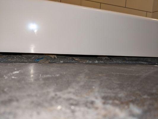 Gap under the edge of the tub with debris.