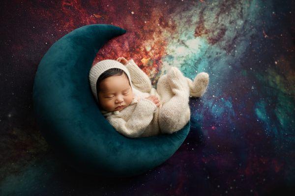 Newborn posed on boom prop with galaxy backdrop for newborn photoshoot in San Diego