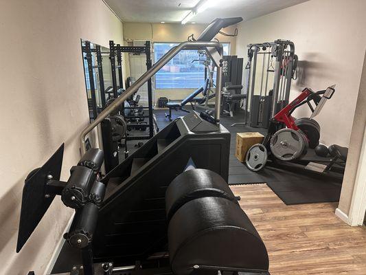 Picture of most of the gym's equipment: squat rack, leg press, stairmaster, cable crossover, and more additions on the way.