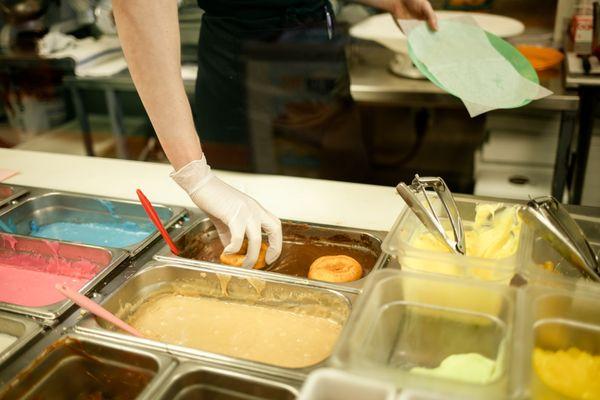 Donuts being dipped in icing right after a customer ordered them