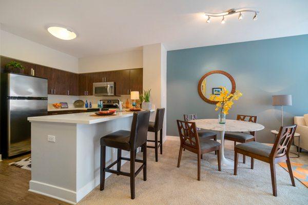 Staged dining area and kitchen with a breakfast bar and stainless steel appliances.