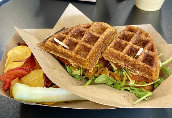 Hummus & Avo BLT Wafflewich: sweet potato waffle, hummus, avo, coconut bacon, smokey mayo, microgreens & tomato + swt potato chips & pickle.