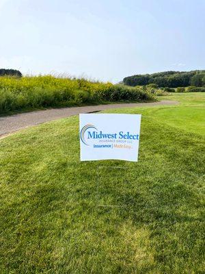 Midwest Select Insurance Group - Insurance Made Easy sponsorship poster surrounded by bright green grass on a sunny Wisconsin summer day.